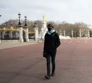 Man in a black coat and a Covid mask walking around Buckingham palace